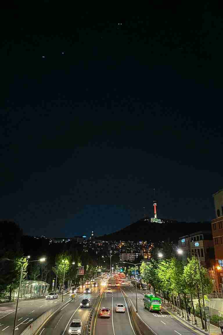 A nighttime view of the Namsan Tower in the far background with cars coming and going on the street