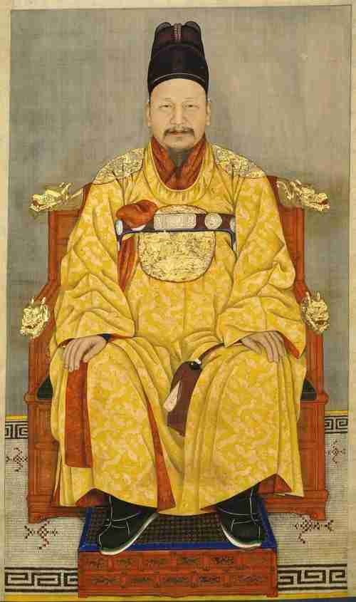 A portrait of Emperor Gojong in a golden traditional Hanok worn by the kings of Joseon. Both his hands are perched atop his knees.