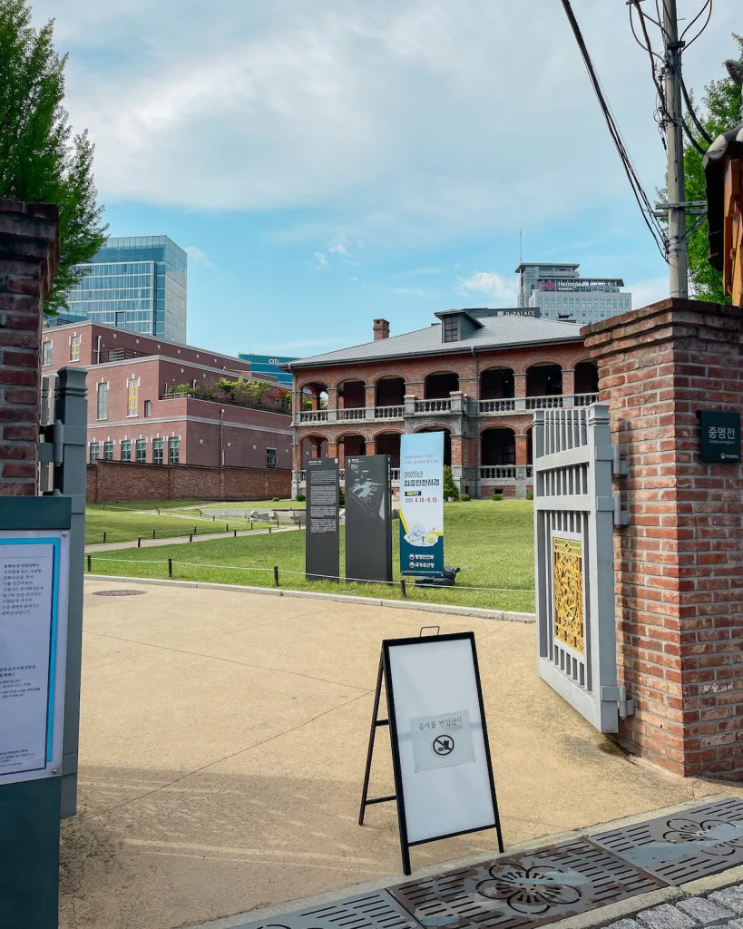 The inconspicuous entrance to  Junmyeongjeon Hall behind Deoksugung Palace, marked by a no food or drink sign, with exhibit banners previewing the historical significance of this royal library.