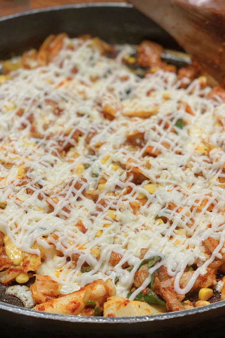 A sizzling skillet of Korean stir-fried chicken (dak galbi) topped with melted cheese and a mix of vegetables like cabbage and corn, showcasing a classic dish enjoyed when dining in Korea. The vibrant orange sauce and stretchy cheese highlight the bold, flavorful cuisine of Korean dining culture.