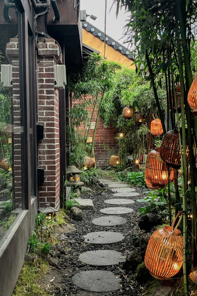 Charming outdoor pathway of a cafe in Seoul, lined with lush bamboo plants and warm, glowing lanterns, creating a cozy and inviting ambiance. Featured in a blog post listing the 10 best cafes to visit in Seoul.