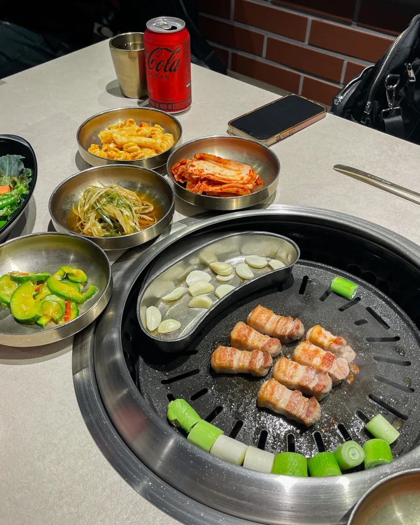 Korean pork belly grilled with garlic and scallions, paired with various side dishes like kimchi and cucumber salad. A classic samgyeopsal meal that defines what to eat in Seoul.