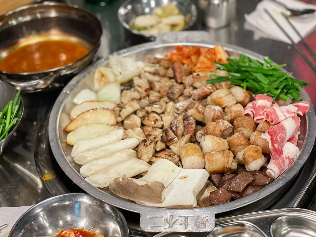 A sizzling platter of gobchang—grilled small intestines—surrounded by garlic, mushrooms, kimchi, and beef slices, served at a Korean barbecue restaurant. 