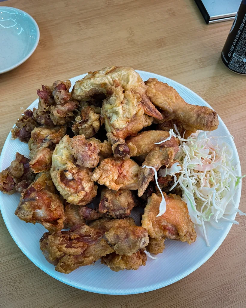 A heaping plate of golden Korean fried chicken, juicy on the inside, served with a small portion of cabbage slaw on the side.