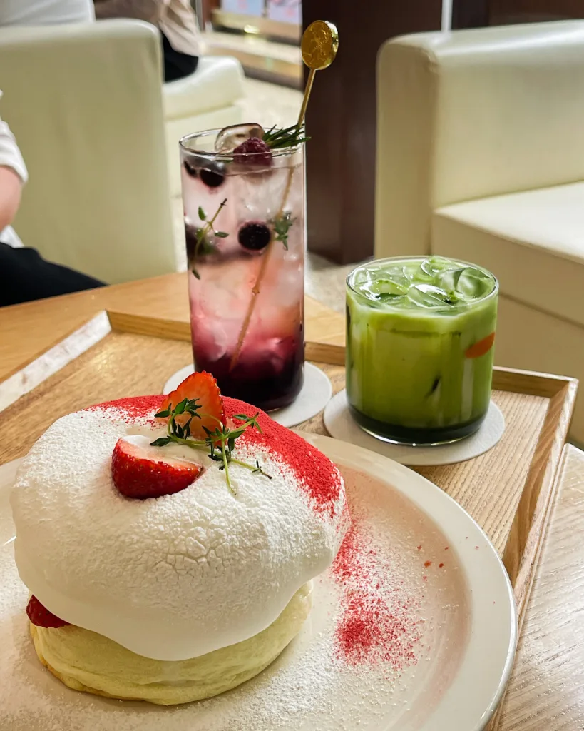 Soufflé pancakes topped with icing sugar and cut strawberries at Onhwa Cafe in Ikseondong Hanok Village in Seoul, served with a glass of iced Matcha Latte and a berry soda.