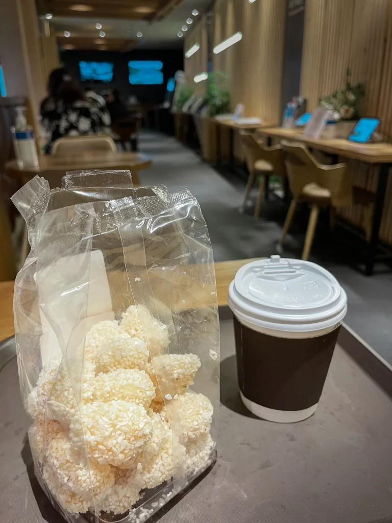 A bag of yugwa—light, airy rice puffs dusted with lightly-sweetened rice flakes—paired with a cup of hot tea in a serene modern café. This nostalgic snack offers a delicate finish to your journey through what to eat in Seoul.