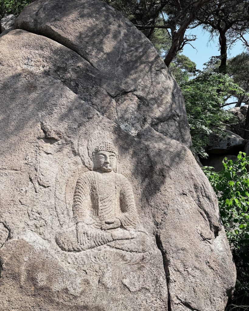 Seated Buddha carved directly into a large granite boulder near the Yongjangsa Temple Site on Mount Namsan in Gyeongju, surrounded by pine trees.