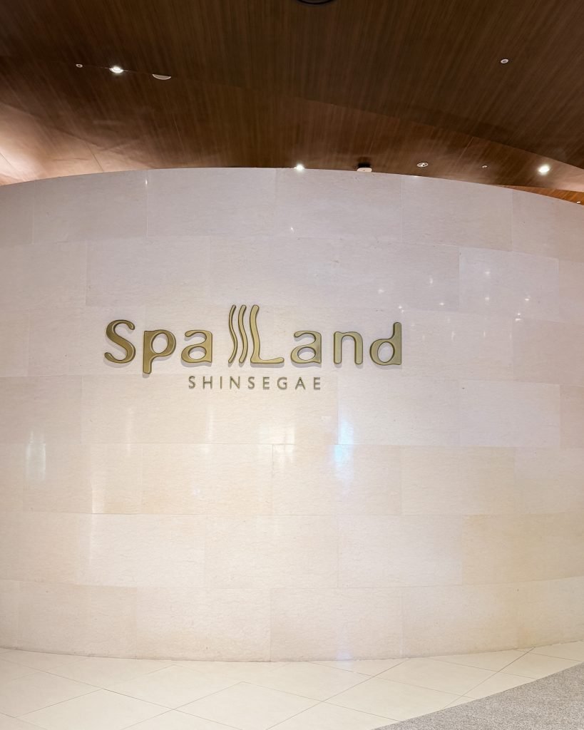 Entrance wall at Spa Land features the words "Spa Land" in elegant lettering above a softly lit stone surface. Busan's luxury jjimjilbang is a popular place to unwind before the end of a trip.