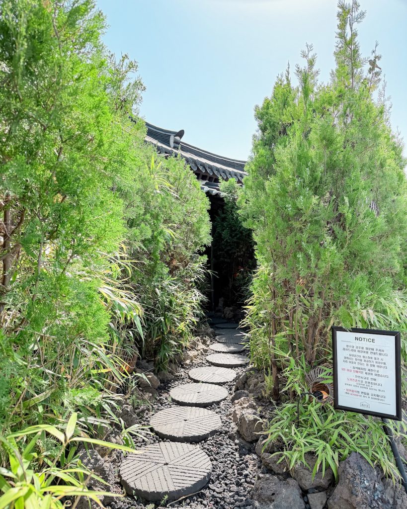 Stone stepping path lined with lush greenery leading to the hidden entrance of Cheongsudang Gyeongju. The secluded garden approach gives the cafรฉ a quiet, tranquil feel before you even step inside.