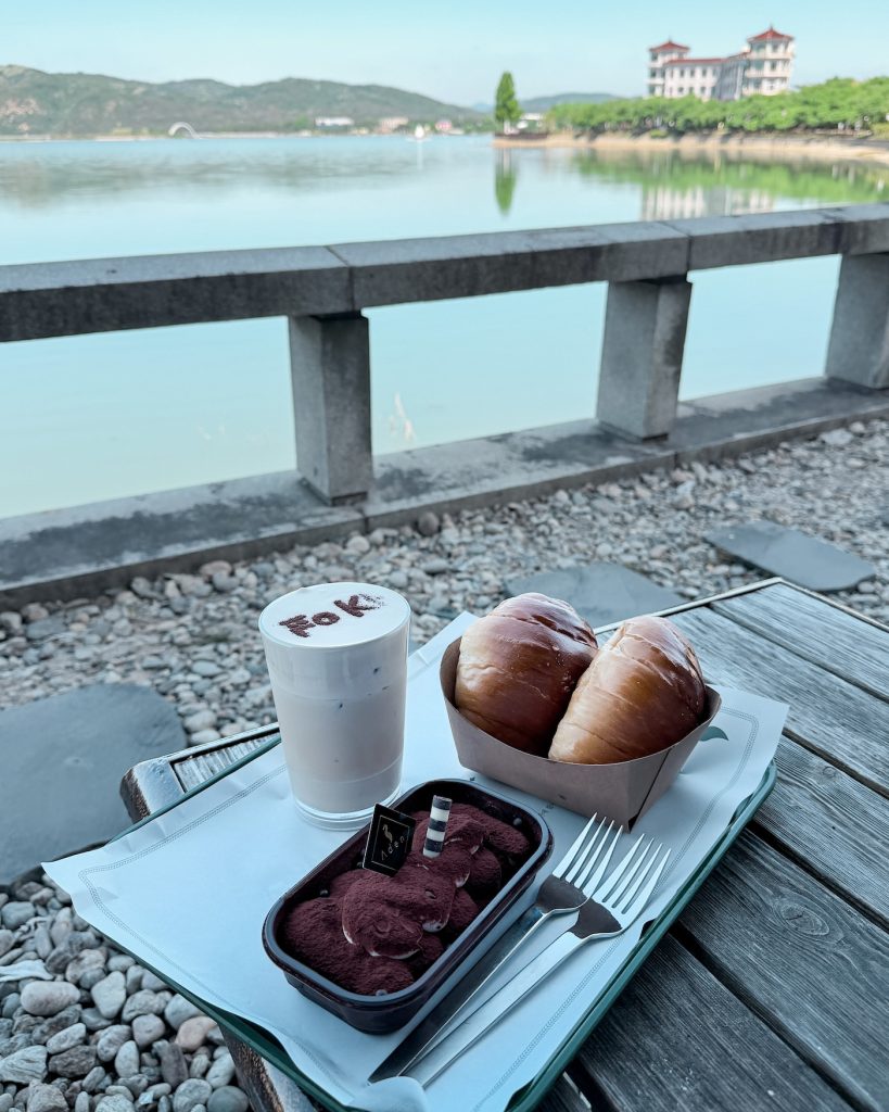 Tiramisu, two salt breads, and an iced peanut butter latte served on an outdoor table overlooking the calm waters of Bomun Lake. The lakeside seating is one of the highlights of visiting Cafe Aden.
