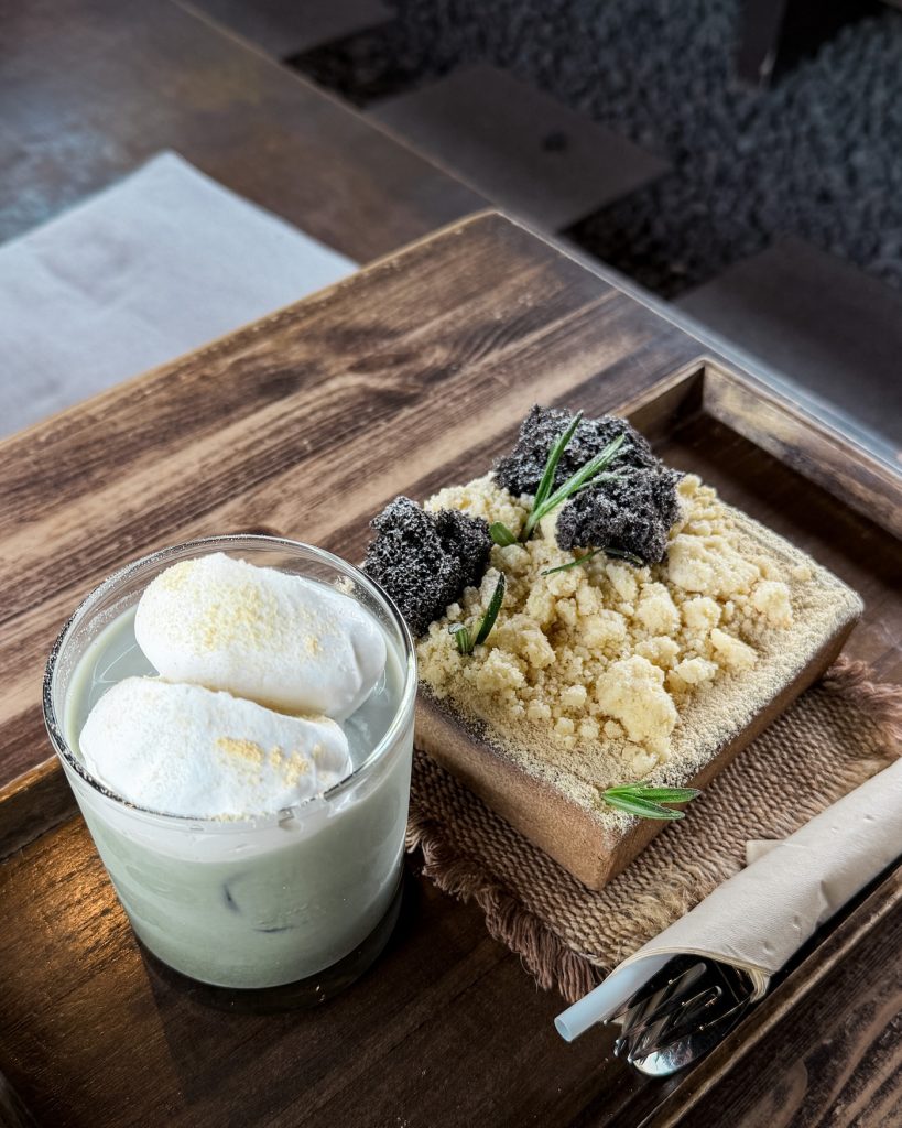 A creamy fromage cake served with injeolmi and black sesame crumble and a wormwood milk topped with whipped cream at Cheongsudang cafe in Gyeongju. The plated dessert and drink showcase a modern Korean cafรฉ presentation.