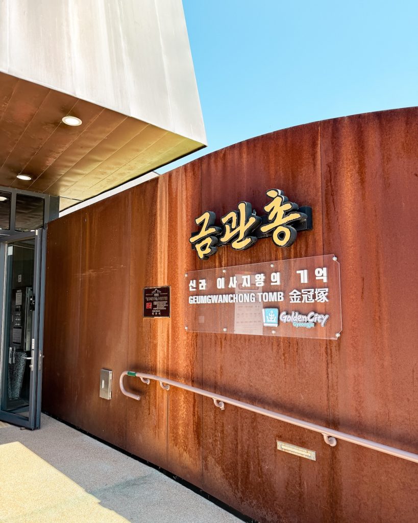 Wooden entrance wall displaying the Geumgwanchong Tomb museum sign at the entrance to one of Gyeongju's royal Silla burial sites. This is the first stop for learning how ancient Silla tombs were constructed and excavated.