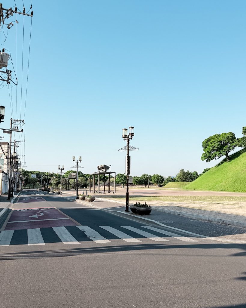 Quiet street in central Gyeongju during the early morning with Geumgwangchong and Daereungwon parks visible in the distance under a clear blue sky.