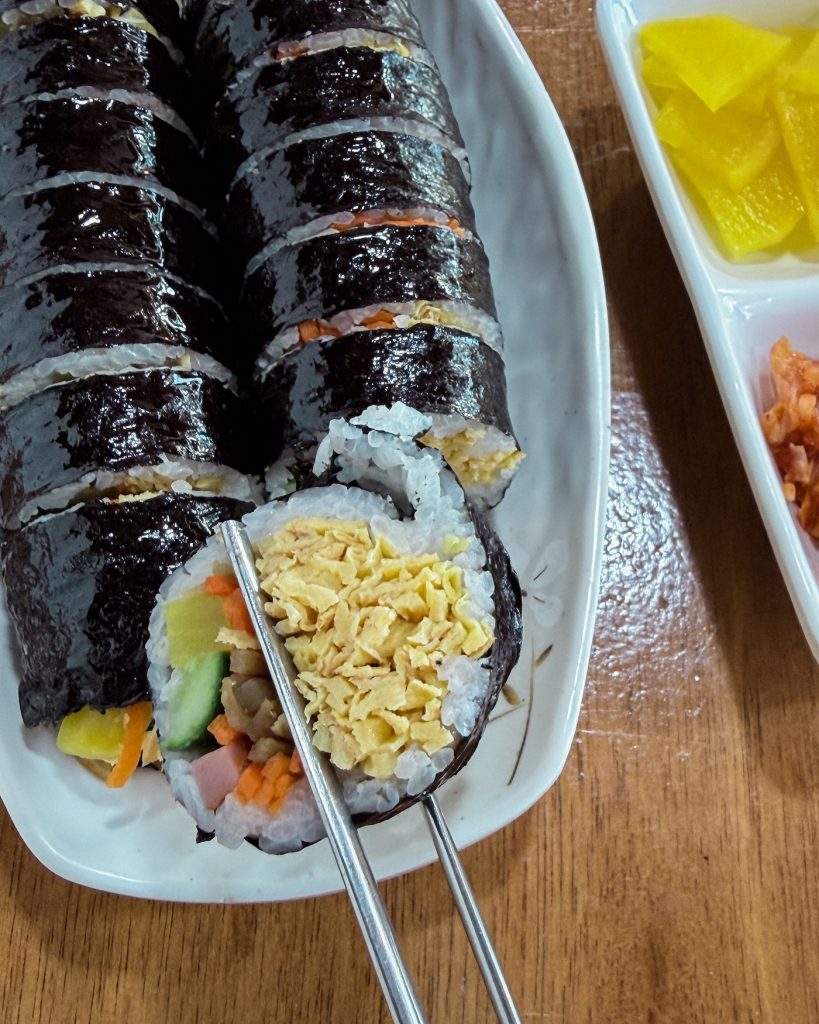 Sliced Gyeongju-style gimbap served with yellow pickled radish, showing its signature filling packed with finely shredded egg. This local specialty makes an easy breakfast or brunch before exploring the nearby royal tombs.
