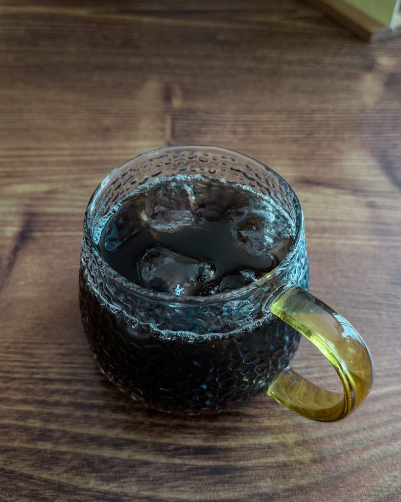 Glass mug of iced ssanghwa cha, a traditional Korean herbal tea, served over ice on a wooden table.