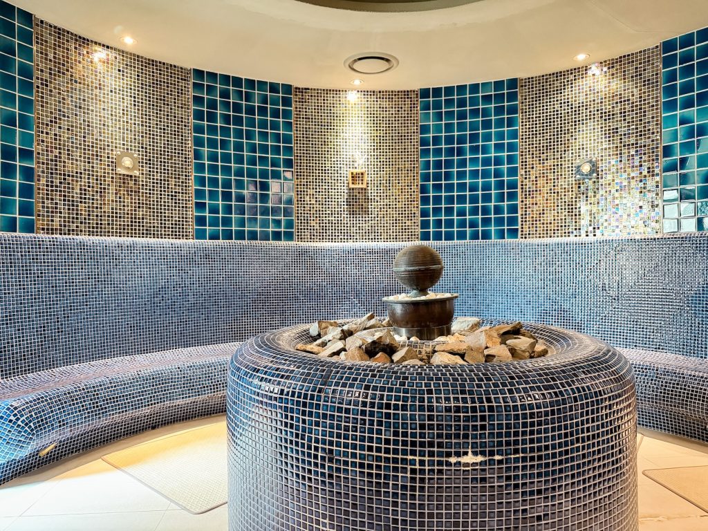 Circular Roman-style sauna at Spa Land features a central stone fountain surrounded by warm mosaic walls and soft ambient lighting. One of several themed sauna rooms designed for relaxation inside the spa complex.