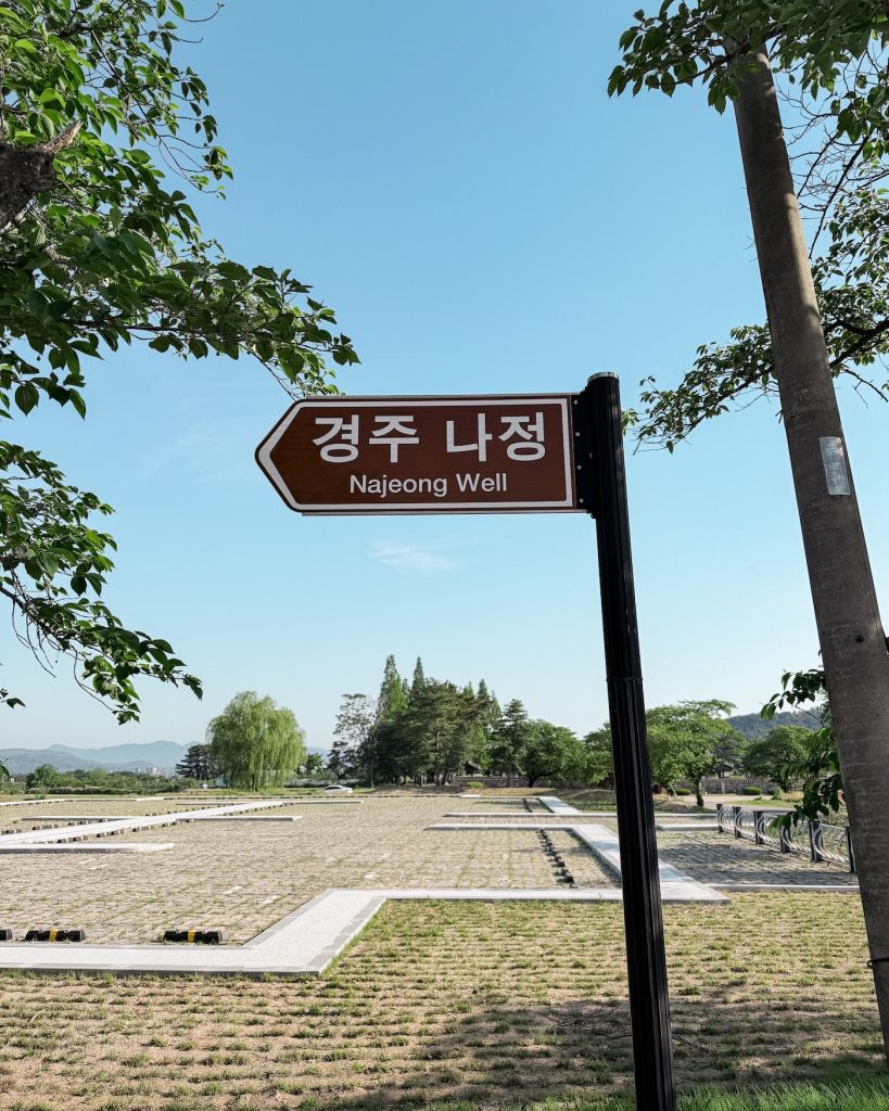 Brown directional sign pointing to Najeong Well with parts of the historic site visible in the background.