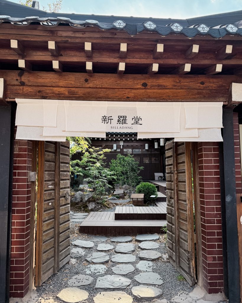 The entrance gate to Silladang opens onto a tranquil courtyard with stone paths, wooden decks, and landscaped greenery. The traditional hanok setting creates a welcoming first impression.