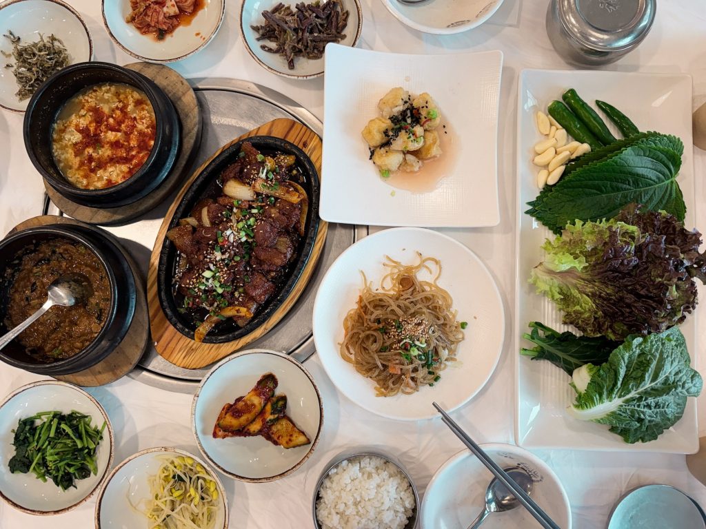 Traditional Korean ssambap meal with numerous side dishes, grilled meat, fresh vegetables, and sauces arranged across a restaurant table at Jinmi Sikdang. This classic Gyeongju lunch is perfect after a morning hike on Mount Namsan.