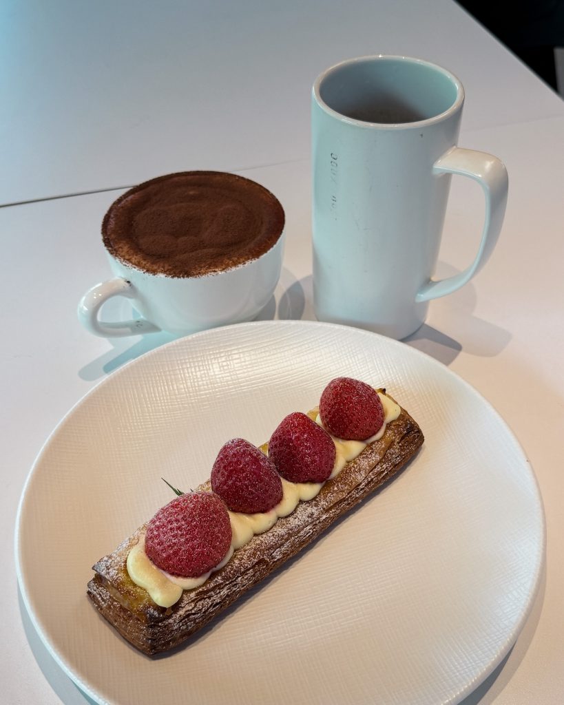 A strawberry Danish topped with fresh strawberries and cream is served alongside a cocoa dusted coffee and a mug at Doux Foret cafรฉ in Gyeongju. The pastry and coffee make a popular cafรฉ pairing.