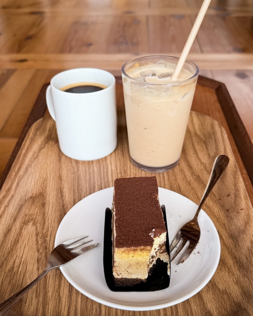 A slice of tiramisu is served with hot black coffee and an iced latte on a wooden tray at TERAROSA in Gyeongju.