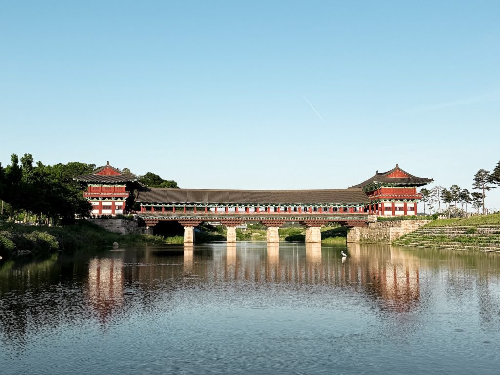 Woljeonggyo Bridge stretches across the river with its colorful wooden pavilions reflected in the water beneath a clear sky. The reconstructed Silla bridge is one of Gyeongju's most recognizable landmarks and a favorite photography spot.