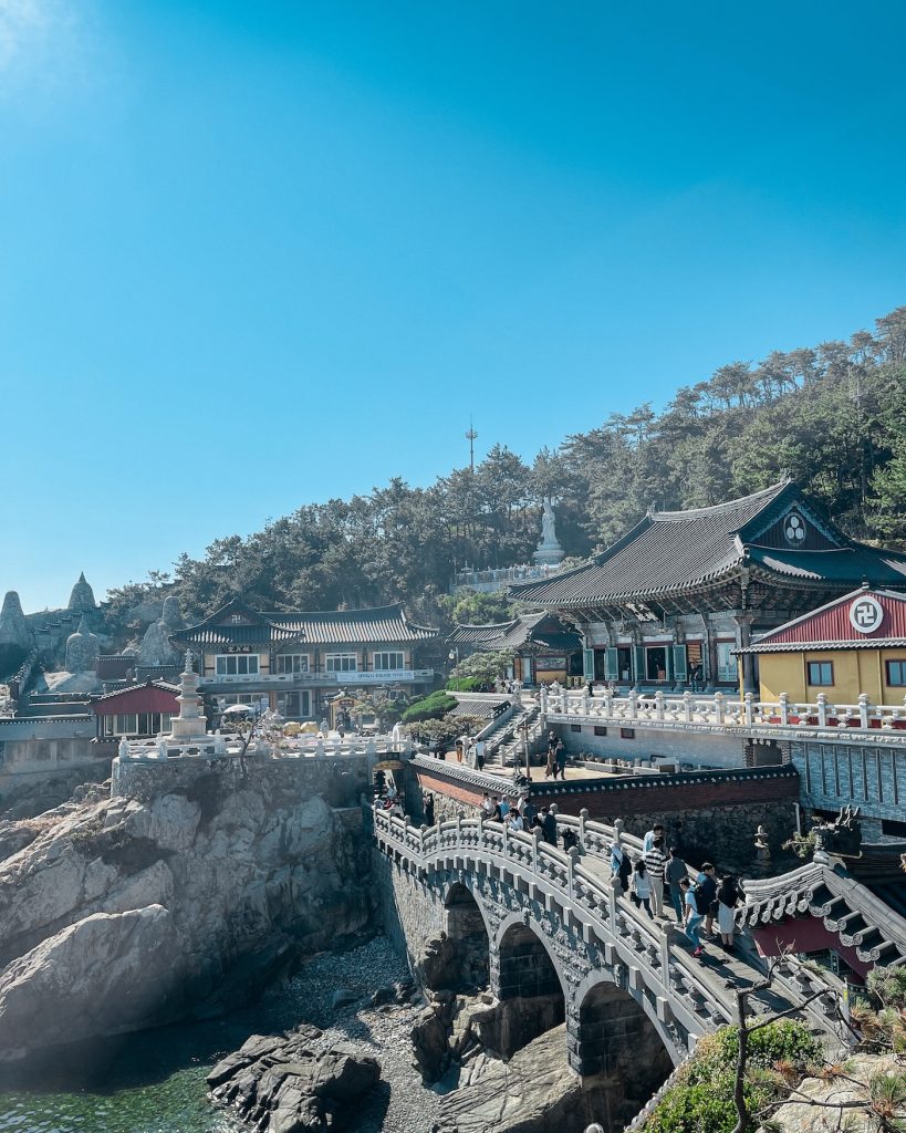 Haedong Yonggungsa Temple sits dramatically on rocky coastal cliffs with ornate bridges, traditional buildings, and the East Sea stretching beyond. Its oceanfront setting makes it one of Busan's most distinctive Buddhist temples.