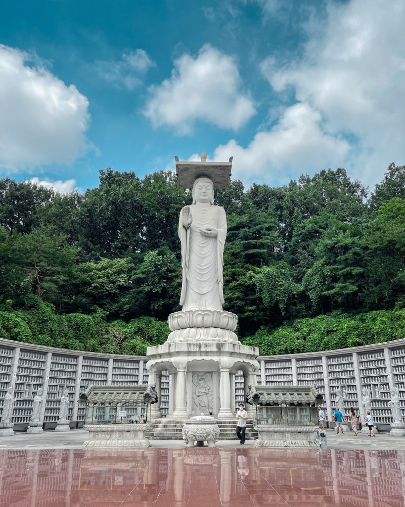 Massive white statue of the future Buddha at Bongeunsa Temple standing above a lotus pedestal and rows of smaller Buddhist figures. The historic temple was another stop on the Gangnam private tour.
